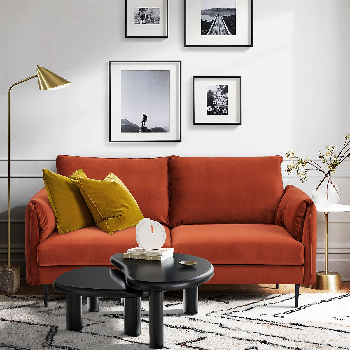 Canapé 3 places en velours terracotta dans un salon moderne, décoré de coussins jaune moutarde, lampadaire doré, tables basses noires et cadres muraux monochromes, ambiance chaleureuse et contemporaine.